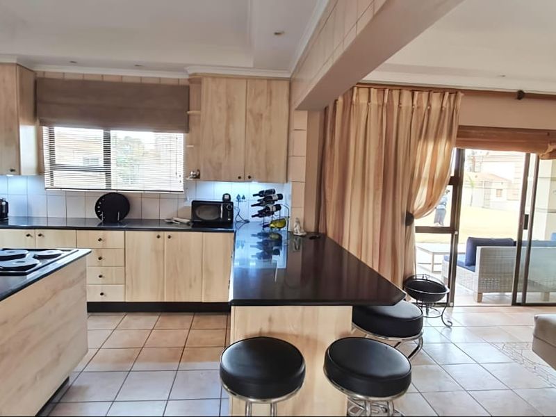 Spacious open-plan kitchen featuring light wood cabinetry, granite countertops, a central island with a built-in hob, and seamless flow to the outdoor patio area.