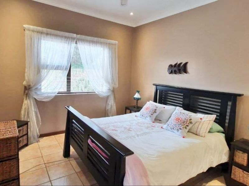 A well-proportioned bedroom featuring neutral wall tones, tiled flooring, and a window with integrated blinds, providing a comfortable and functional living space.