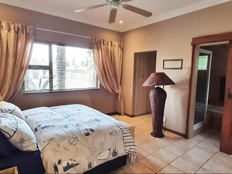 A spacious bedroom featuring tiled flooring, a ceiling fan, and a sliding wooden door leading to an en-suite bathroom.