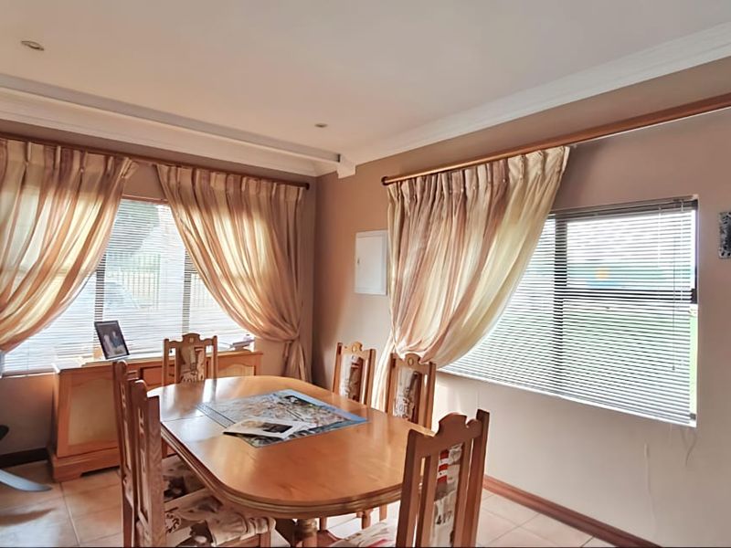 A dining room featuring tiled flooring, recessed downlights, and large windows fitted with venetian blinds and curtain rods.