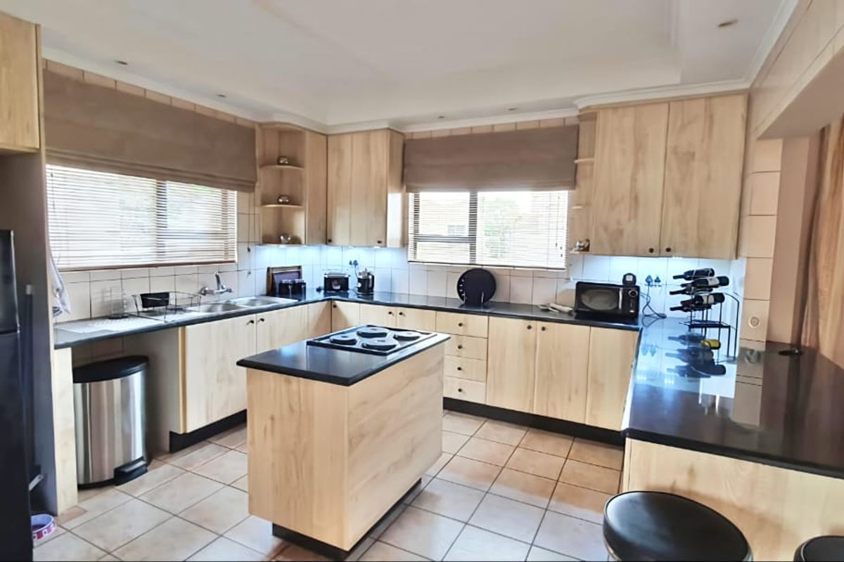 A functional kitchen featuring light wood cabinetry, a central island with a built-in hob, dark granite countertops, and tiled flooring.