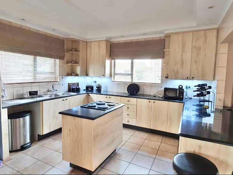 A functional kitchen featuring light wood cabinetry, a central island with a built-in hob, dark granite countertops, and tiled flooring.