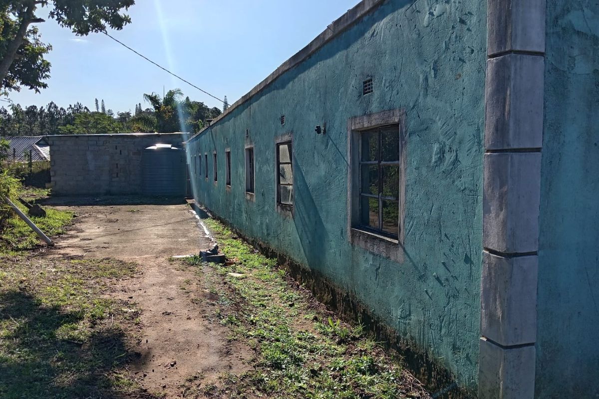 Rear exterior view of the property showing a long plastered wall, concrete pathway, and a water tank in a weathered condition.