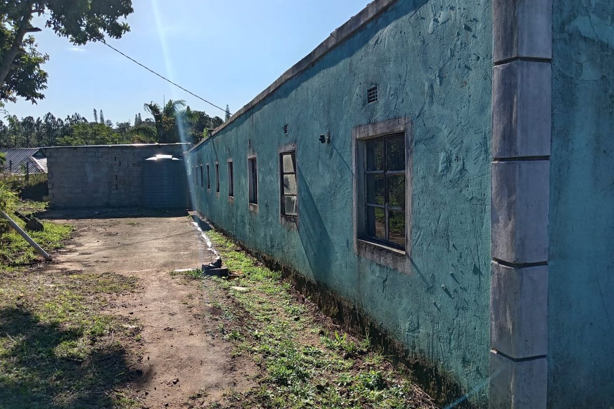 Rear exterior view of the property showing a long plastered wall, steel windows, concrete driveway, and a water tank.