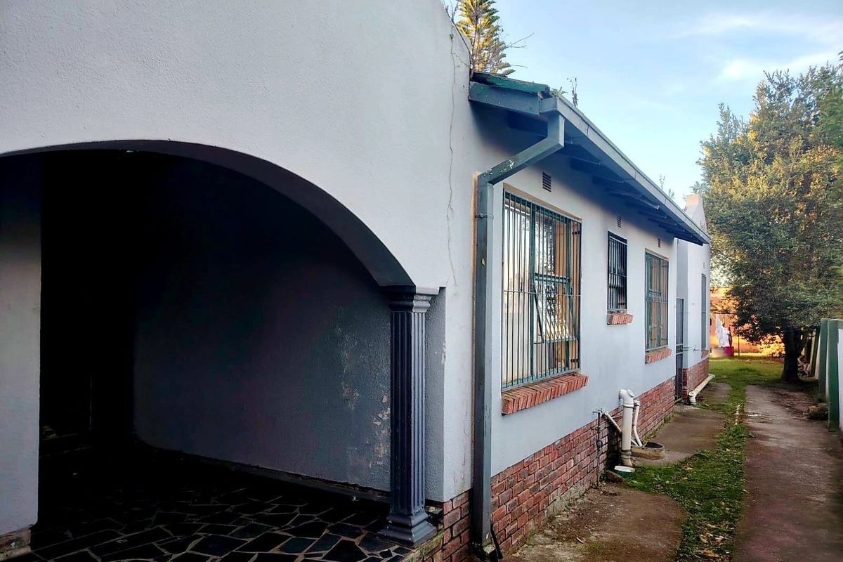 Rear exterior view of the house featuring a covered patio area, brick base detailing, and security bars on the windows.