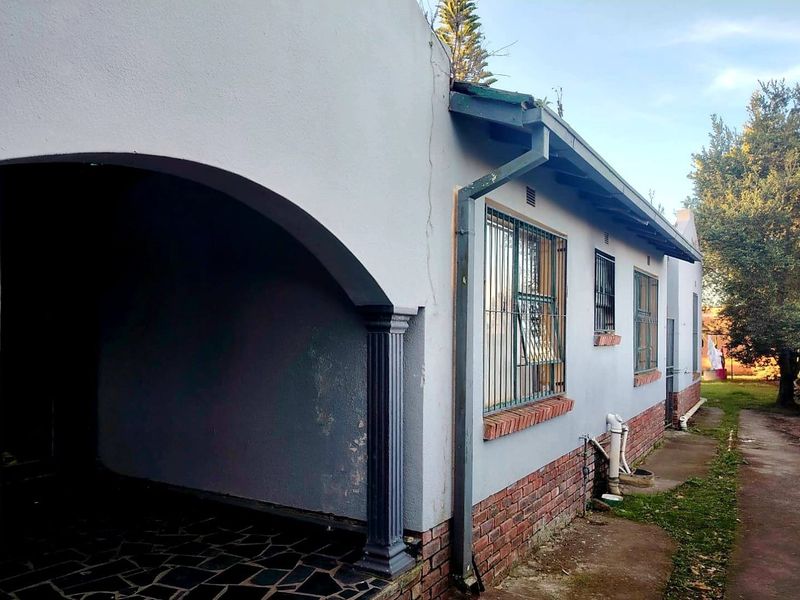 Rear exterior view of the house featuring a covered patio area, brick base detailing, and security bars on the windows.