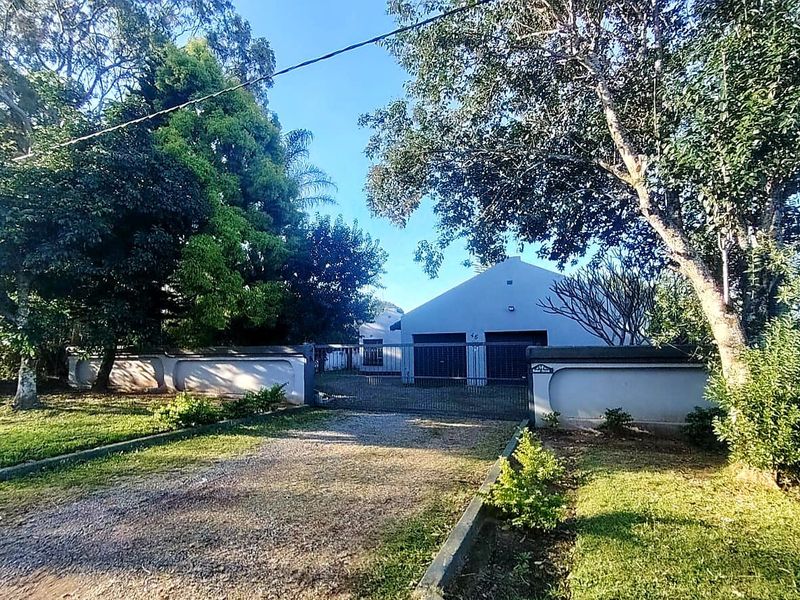 Front view of the property featuring a gravel driveway, secure metal gate, perimeter wall, and a double garage entrance.