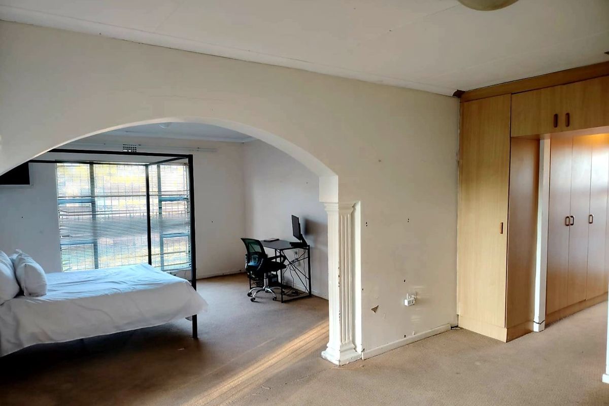 Spacious bedroom featuring built-in cupboards, a decorative archway, and large windows, offering a versatile layout with potential for modernization.