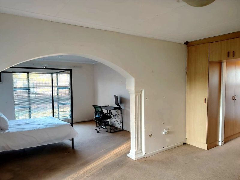 Spacious bedroom featuring built-in cupboards, a decorative archway, and large windows, offering a versatile layout with potential for modernization.