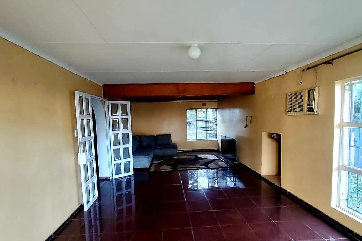 A living room featuring tiled flooring, an exposed timber beam, and a wall-mounted air conditioning unit, with access via french doors.
