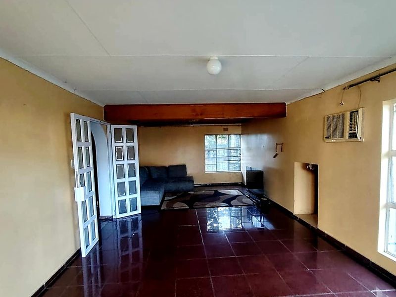 A living room featuring tiled flooring, an exposed timber beam, and a wall-mounted air conditioning unit, with access via french doors.