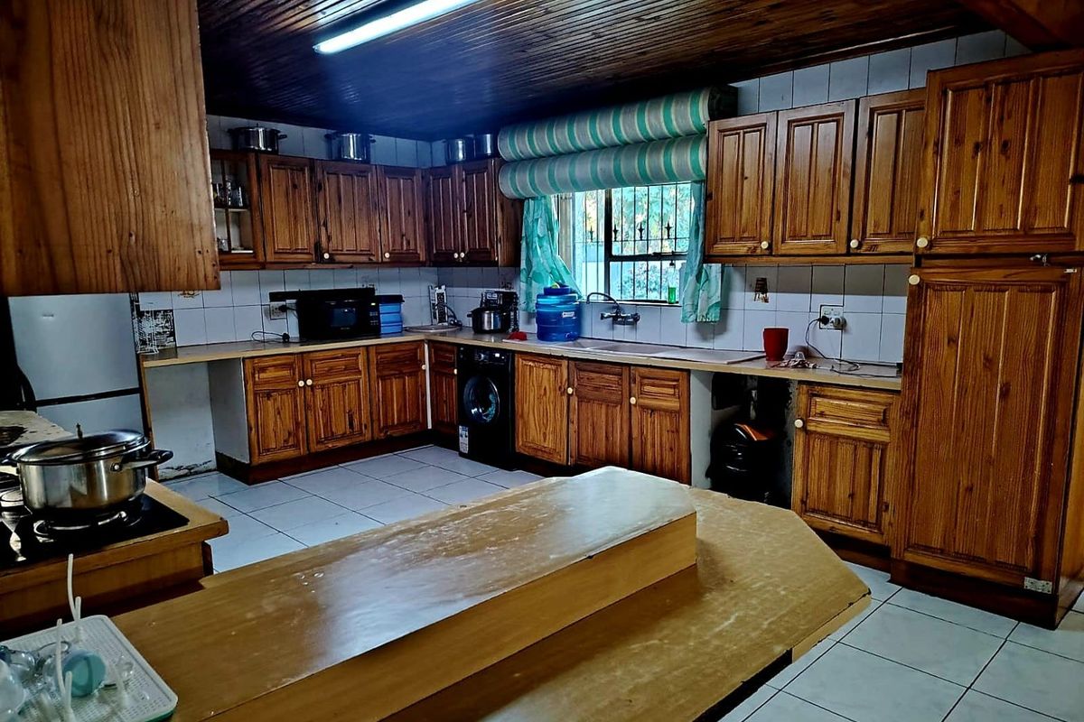 A spacious kitchen featuring extensive wooden cabinetry, tiled flooring, a timber ceiling, and a central island, offering a functional layout with classic finishes.