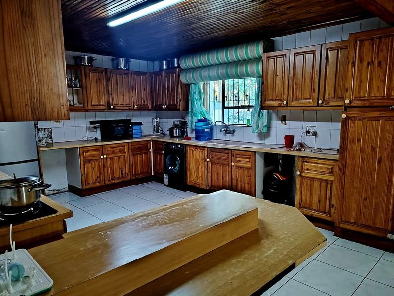 A spacious kitchen featuring extensive wooden cabinetry, tiled flooring, a timber ceiling, and a central island, offering a functional layout with classic finishes.