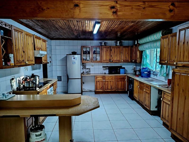 Spacious kitchen featuring extensive wooden cabinetry, tiled flooring, and a traditional wooden ceiling with exposed beam, offering significant potential for modern renovation.