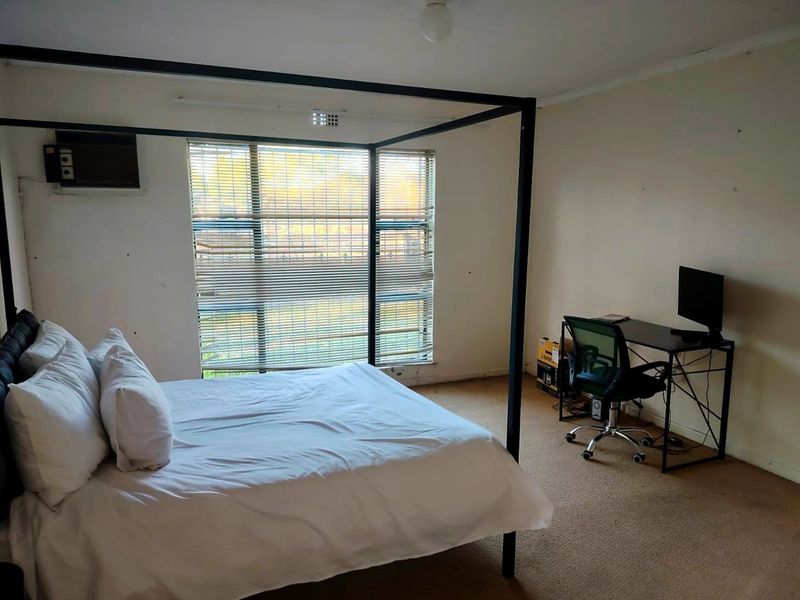 A bedroom featuring carpet flooring, window blinds, and a wall-mounted air conditioning unit.