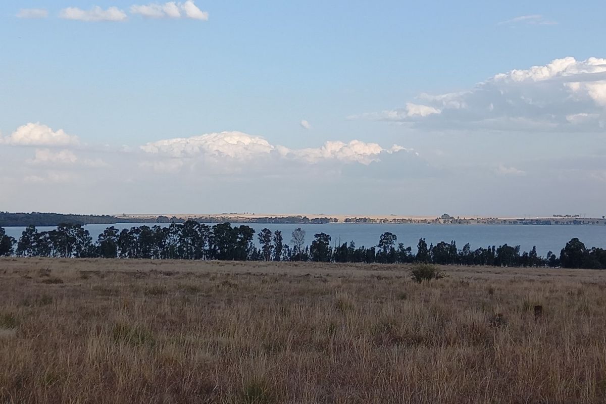 A scenic view of the open landscape featuring natural vegetation and a distant water body under a clear sky.