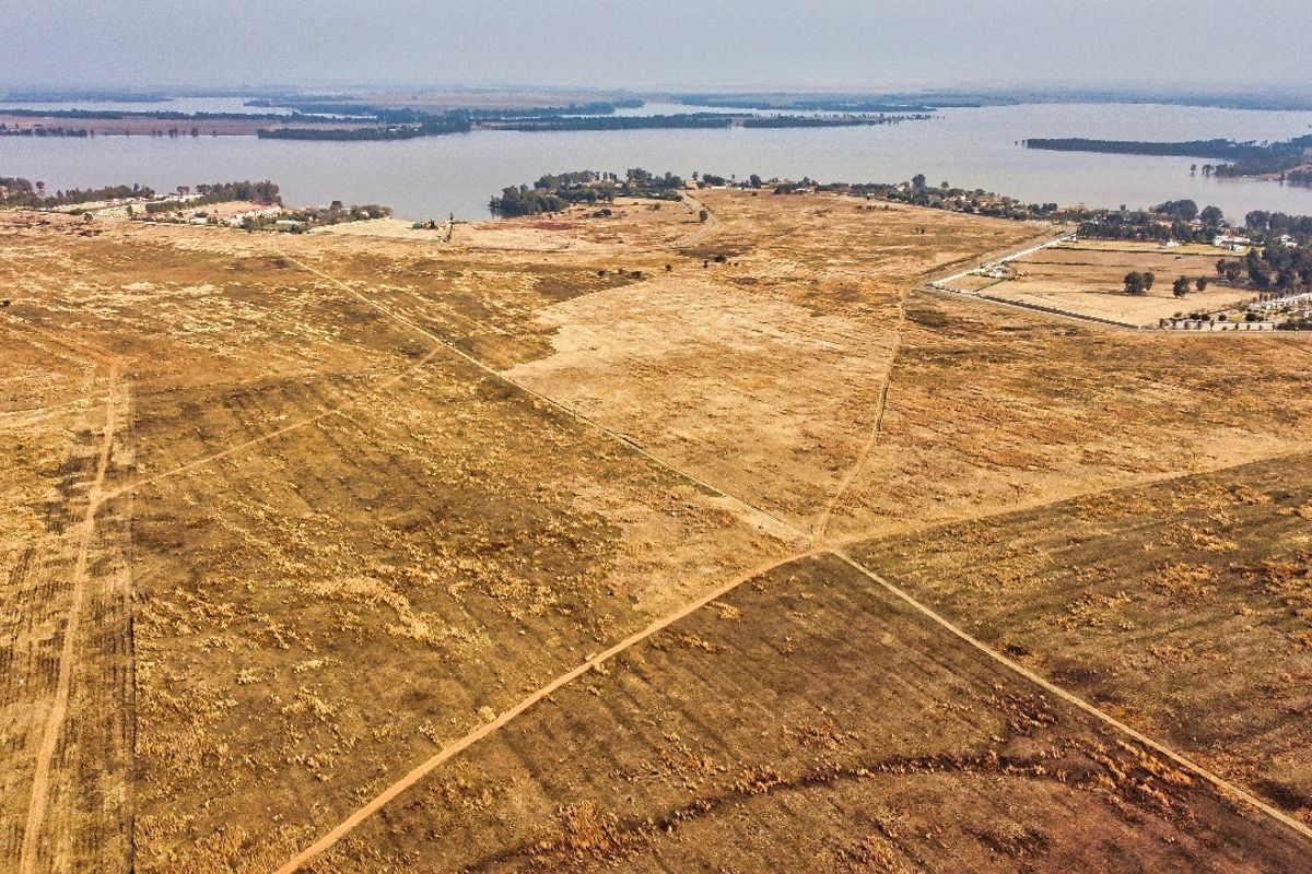 An expansive aerial view of vacant residential land featuring natural terrain and proximity to a large water body.
