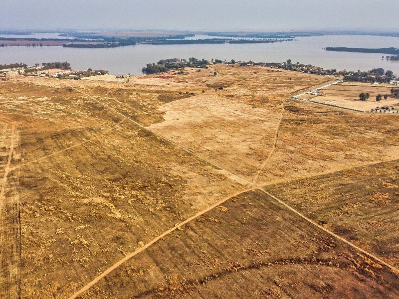An expansive aerial view of vacant residential land featuring natural terrain and proximity to a large water body.