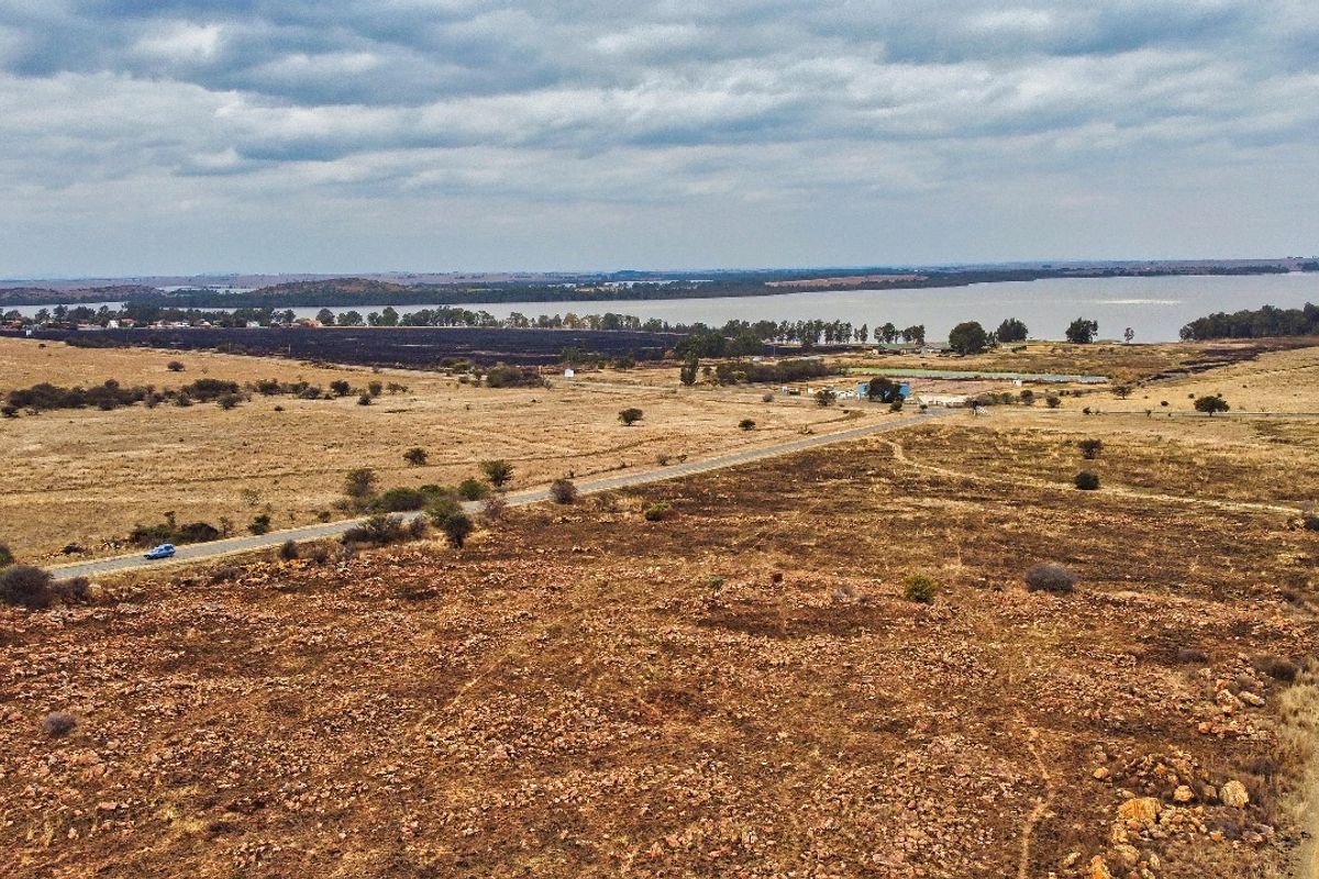 An aerial view of a large, undeveloped residential land parcel featuring natural terrain, gravel access paths, and proximity to a nearby lake.