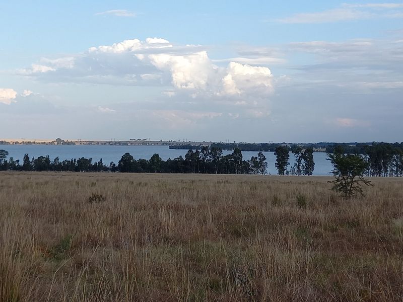 A scenic view of a natural landscape featuring open fields and a distant water body under a cloudy sky.