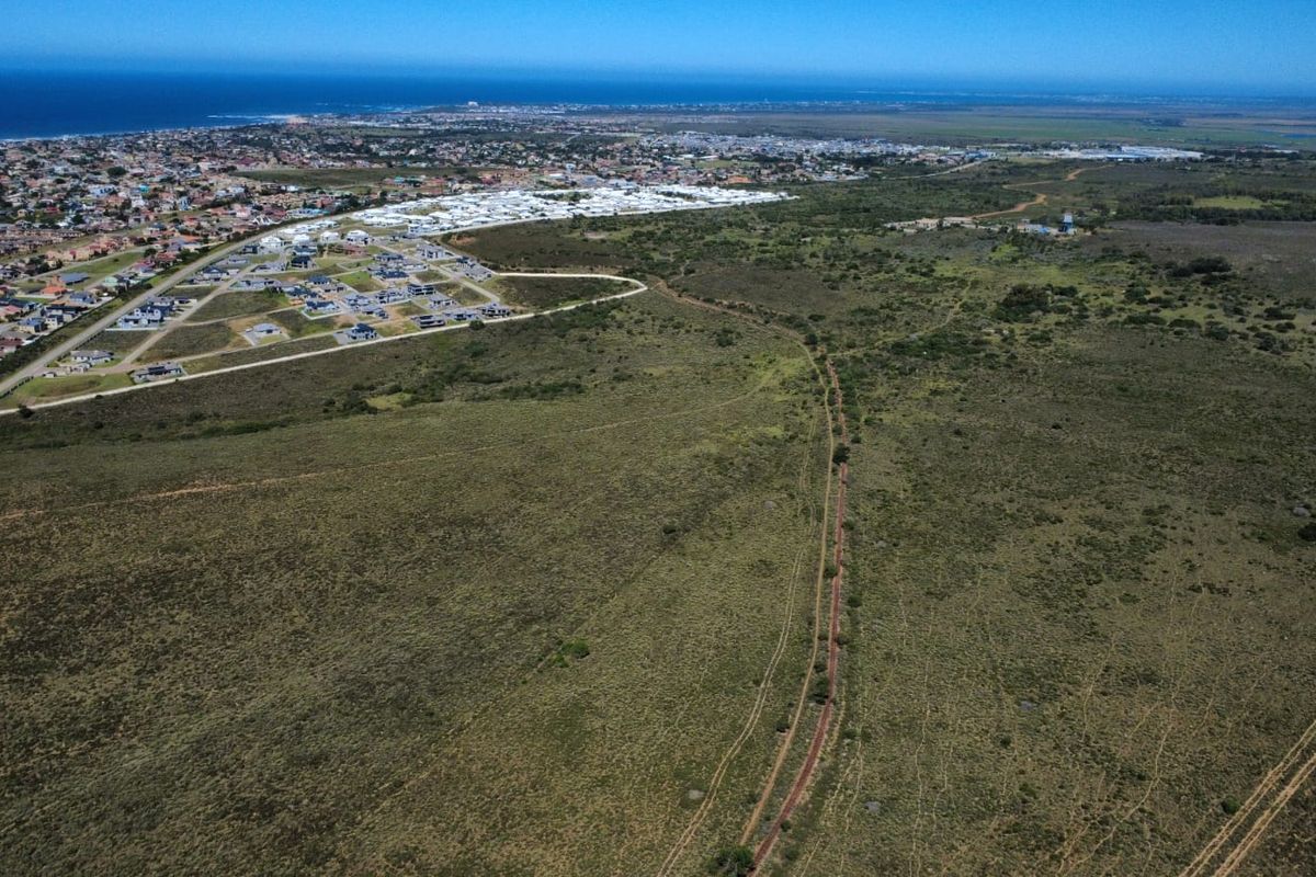 Aerial view of expansive undeveloped farm land with a dirt track, situated near a residential coastal development.
