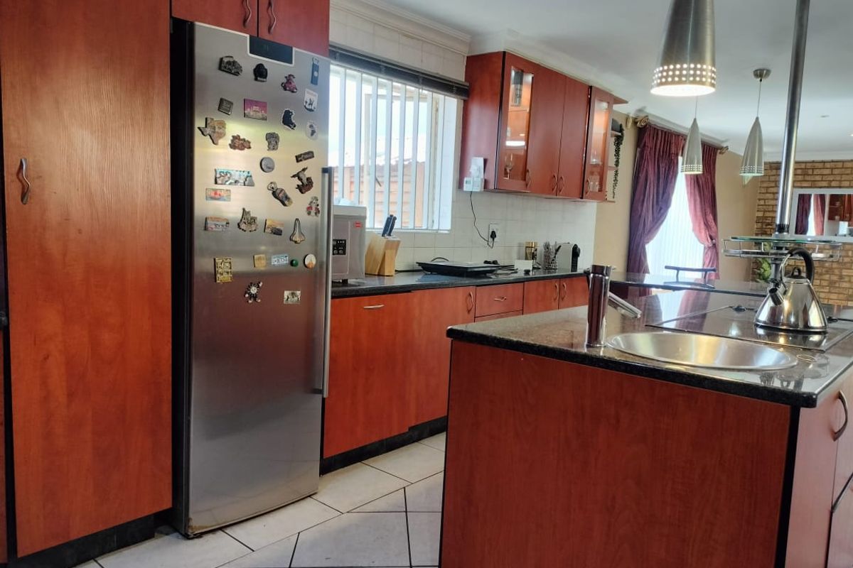 A functional kitchen featuring wood-veneer cabinetry, granite countertops, a central island with a prep sink, and tiled flooring.
