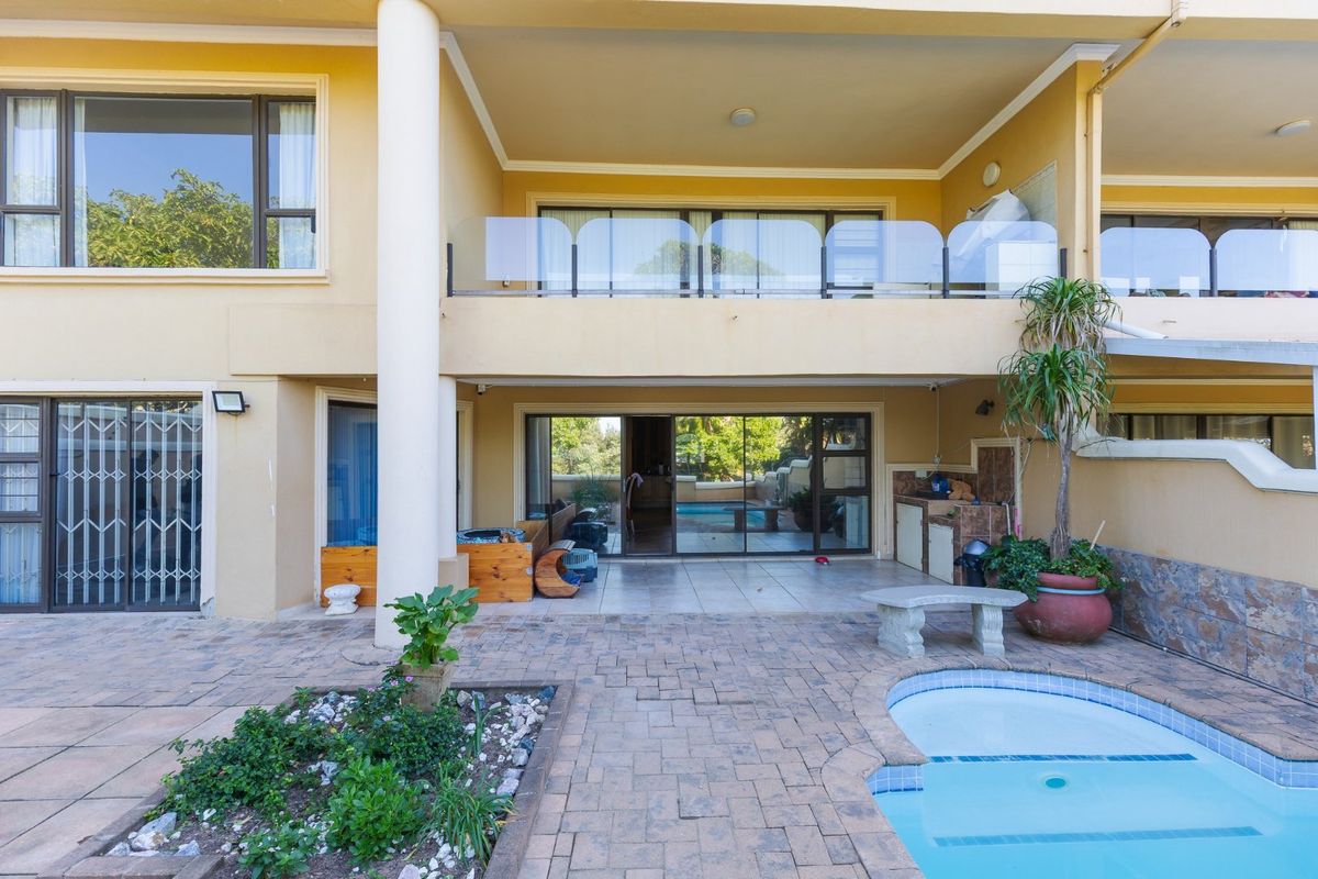 Rear exterior view featuring a paved patio area, a small swimming pool, and a covered balcony with a glass balustrade.
