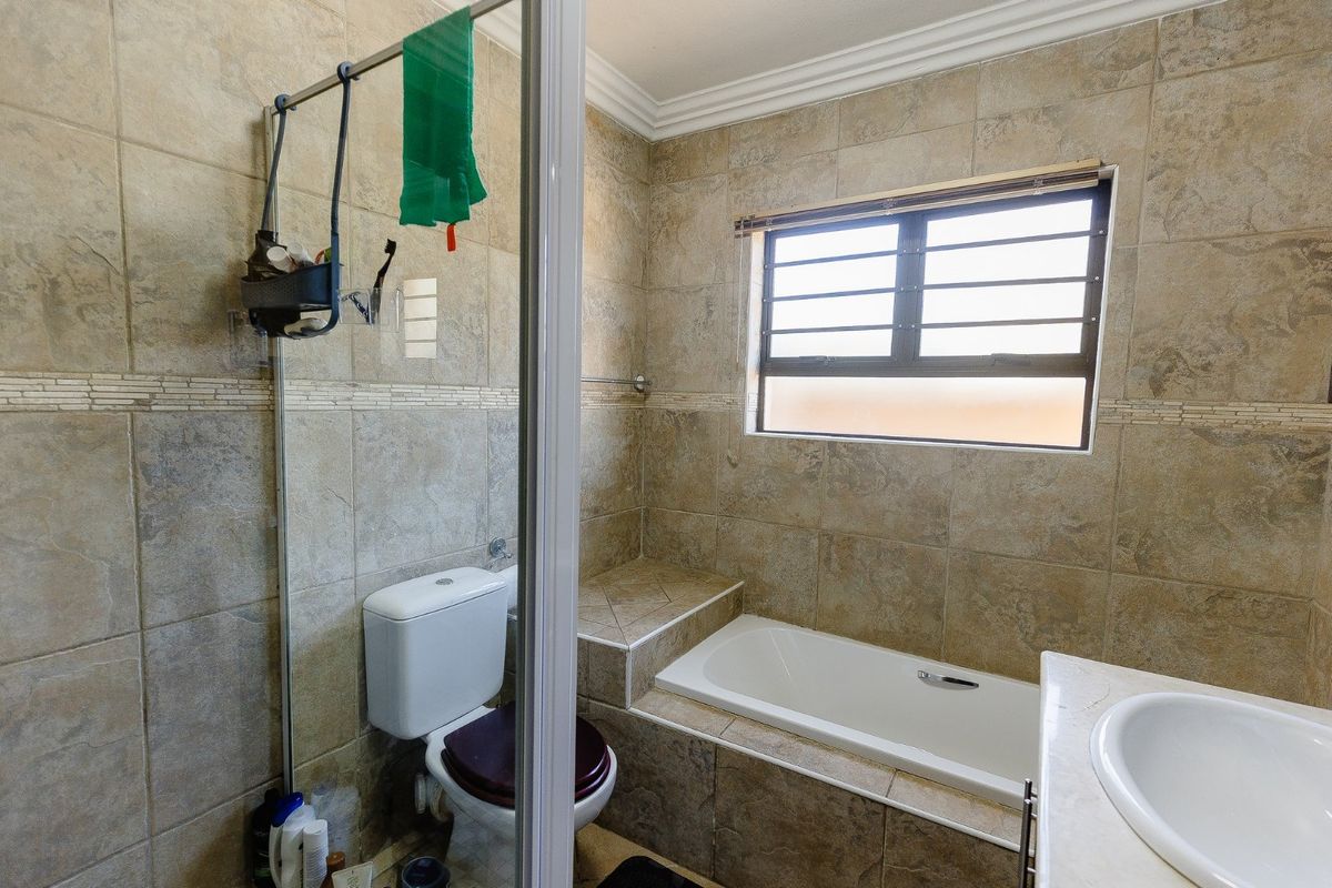 A functional bathroom featuring a built-in bathtub, tiled wall finishes, a vanity basin, and a toilet, with a window providing natural light.