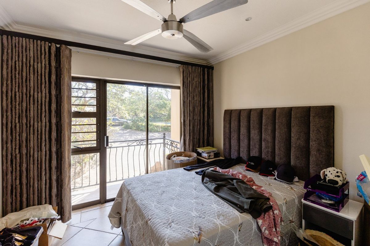 A well-lit bedroom featuring a ceiling fan, tiled flooring, and a sliding glass door providing access to a private balcony with iron railings.