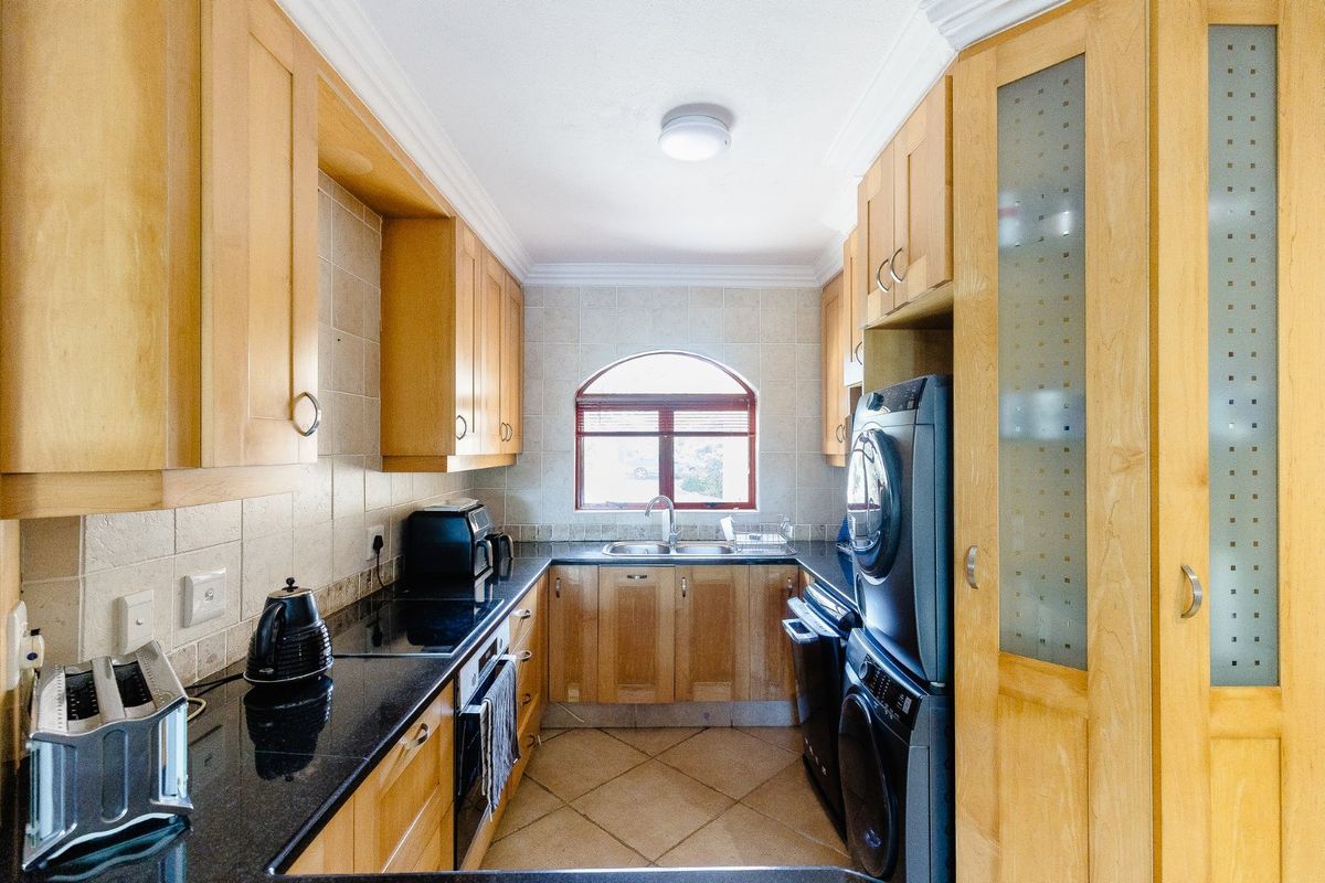 A functional kitchen featuring light wood cabinetry, dark granite countertops, a double basin sink, and tiled flooring with an arched window.