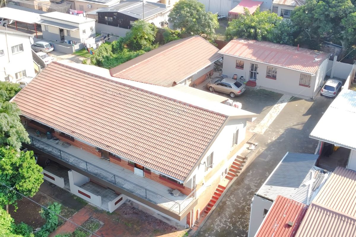 Aerial view of the property showing the main house with a tiled roof, surrounding outbuildings, paved driveway, and established garden areas.