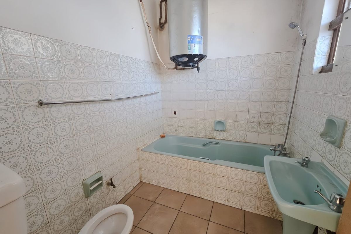A dated bathroom featuring a blue bathtub and pedestal basin, tiled walls, and an exposed electric water heater.