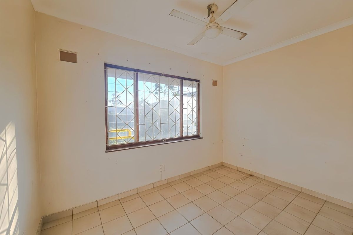 An empty bedroom featuring tiled flooring, a ceiling fan, and a window fitted with security bars.