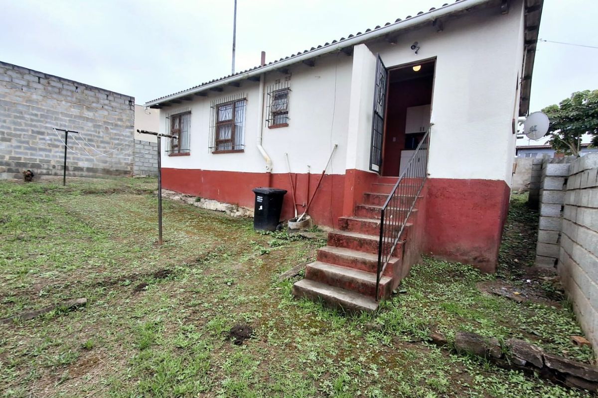 Rear exterior view of the house featuring a concrete staircase, security bars on windows, and a large backyard area with boundary walls.