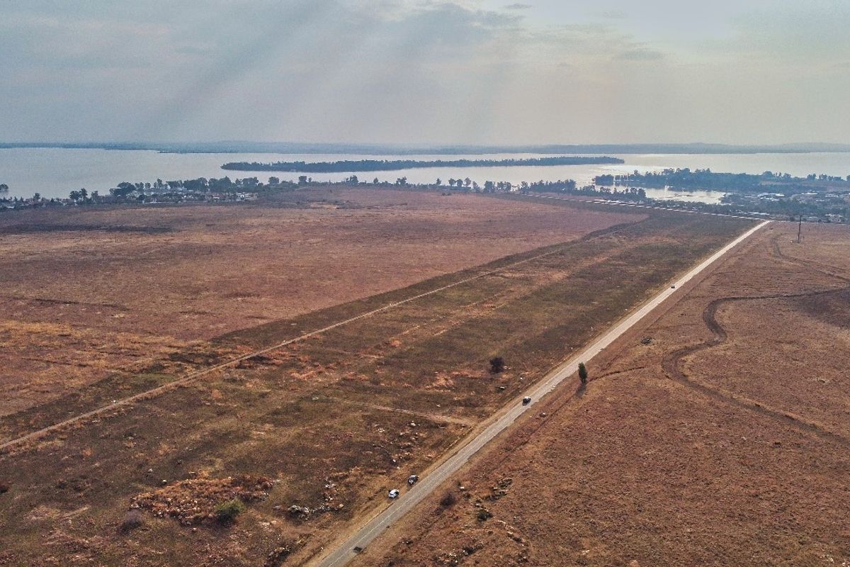 Aerial view of a large, vacant residential land parcel featuring road access and scenic waterfront proximity.