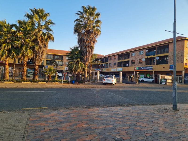 Street view of a multi-story apartment complex featuring brick exterior, balconies, and ground-level commercial storefronts.