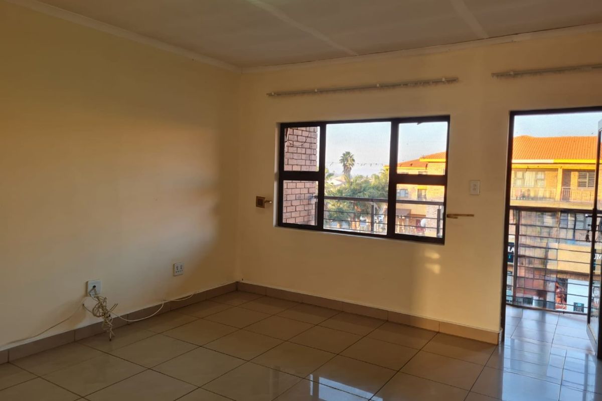 An empty, tiled living area featuring aluminium window frames and a sliding door leading to an outdoor space.