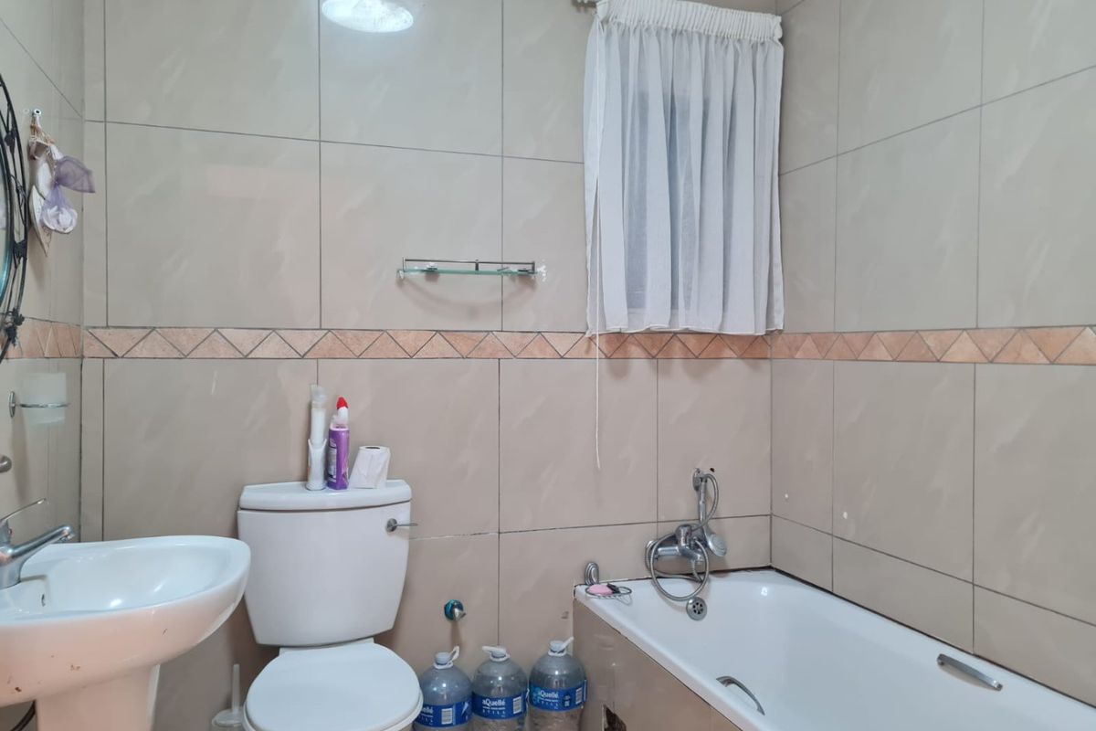 A functional bathroom featuring a pedestal basin, toilet, and bathtub with wall-mounted mixer, finished with neutral ceramic wall tiles.