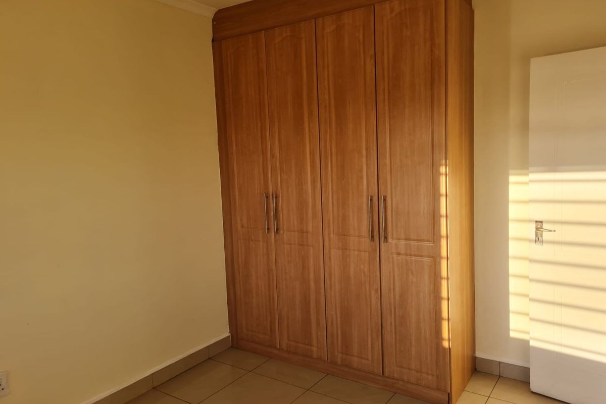 A clean bedroom featuring a large, wood-finish built-in wardrobe and neutral tiled flooring, offering a functional and well-maintained storage solution.