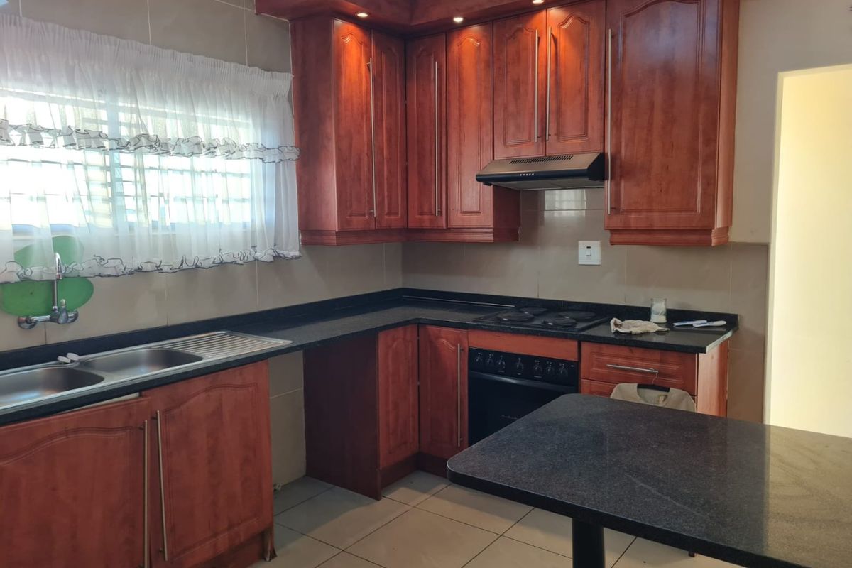 A functional kitchen featuring warm-toned wooden cabinetry, granite countertops, a built-in oven with hob, and a double stainless steel sink.