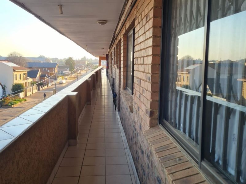 A long, covered balcony featuring tiled flooring and brick exterior walls, offering an elevated view of the surrounding neighborhood.