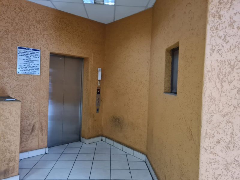 A communal apartment hallway featuring an elevator, intercom system, and tiled flooring with visible wear and wall damage.