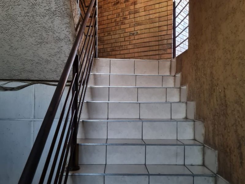 A functional stairwell featuring tiled steps, a metal handrail, and a combination of exposed brick and textured wall finishes.