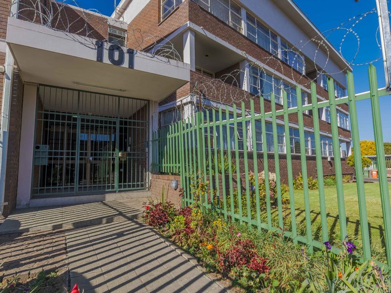 Front exterior view of the apartment building featuring a brick facade, secure gated entrance, and perimeter palisade fencing with razor wire.