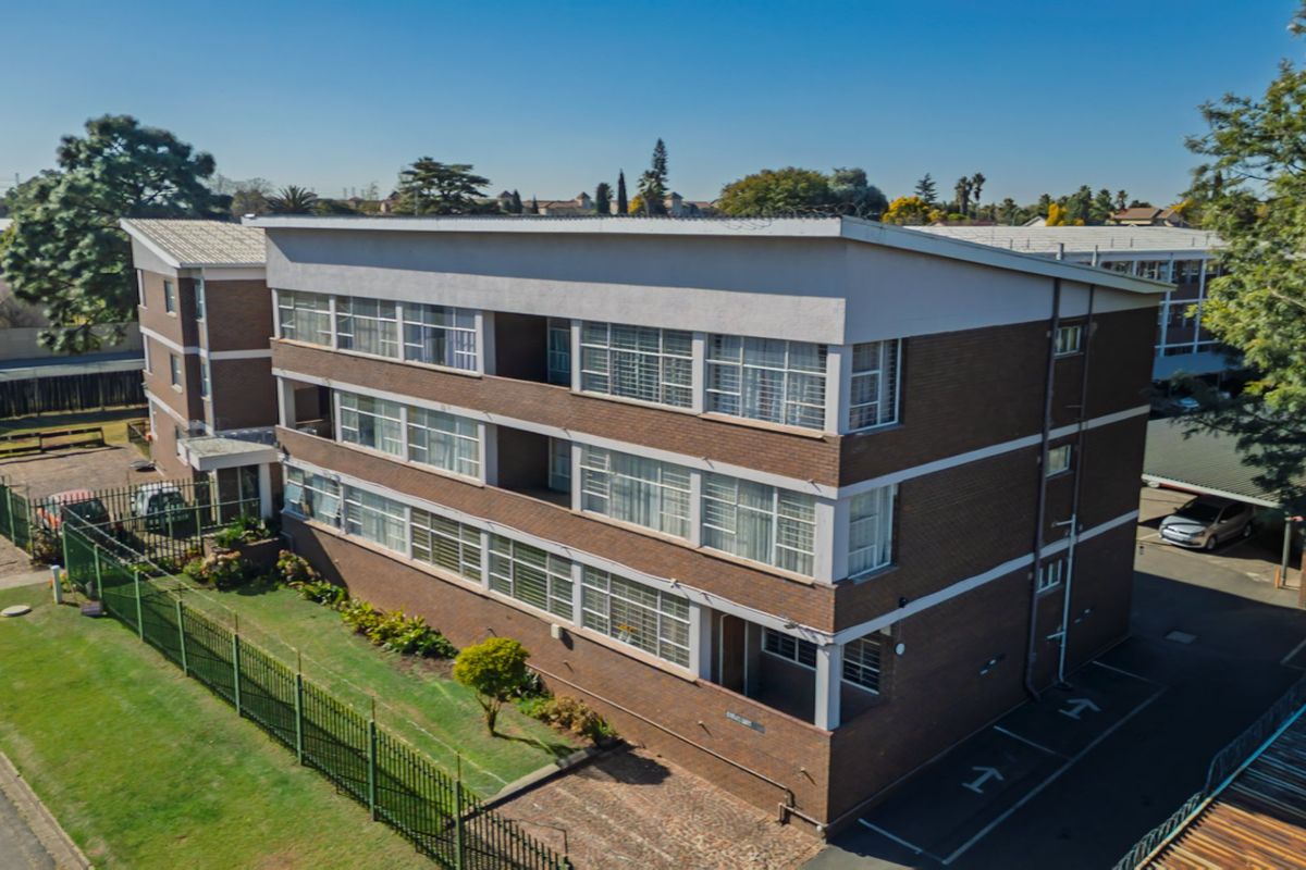Aerial view of a multi-story brick apartment building featuring a metal roof, surrounding security fencing, and an adjacent paved parking area.