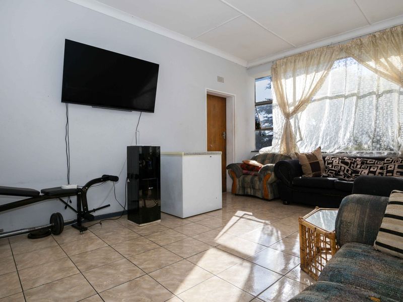 A living room featuring tiled flooring and a coved ceiling, offering a functional space with natural light from the large window.