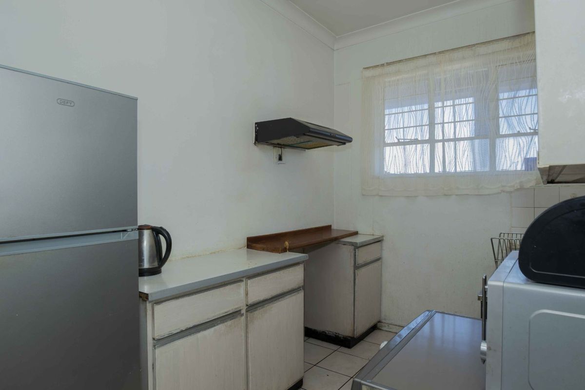 A compact kitchen featuring dated built-in cabinetry, a wall-mounted extractor fan, and tiled flooring, offering potential for a modern renovation.