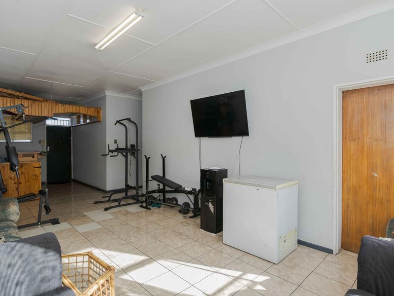 A multi-purpose living area featuring tiled flooring, a timber door, and a timber partition, currently utilized as a home gym space.