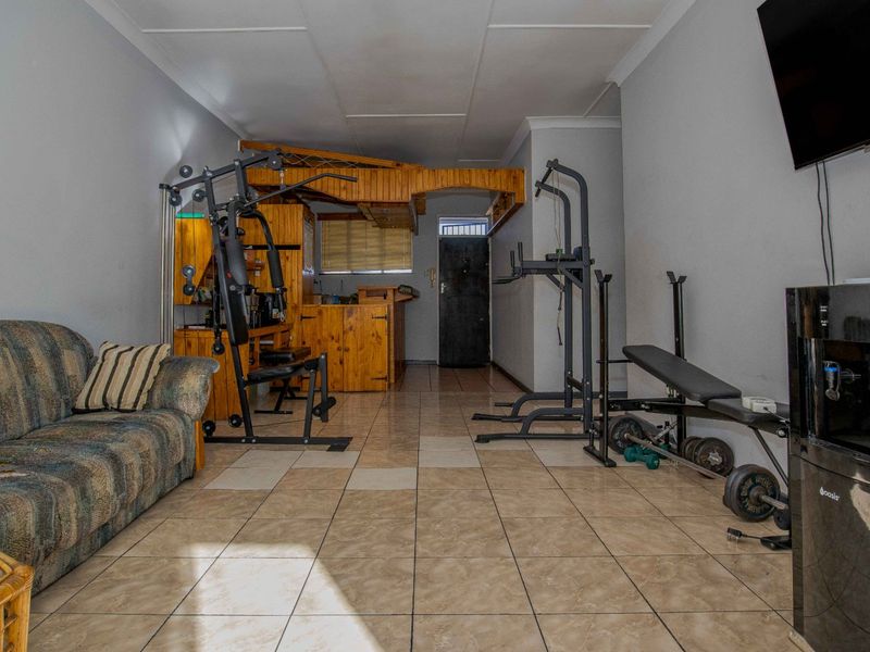 A multi-purpose living area featuring tiled flooring and a built-in wooden bar counter, currently utilized as a home gym space.