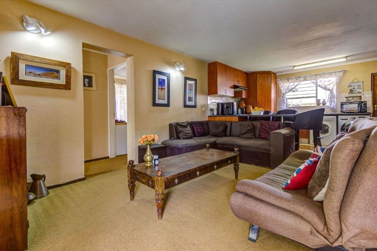 Open-plan living area featuring a combined lounge and kitchen space with dated finishes and carpeted flooring.